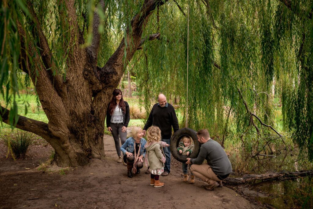 Candid photo of grandparents, son, daughter-in-law and grandchildren playing below a willow tree