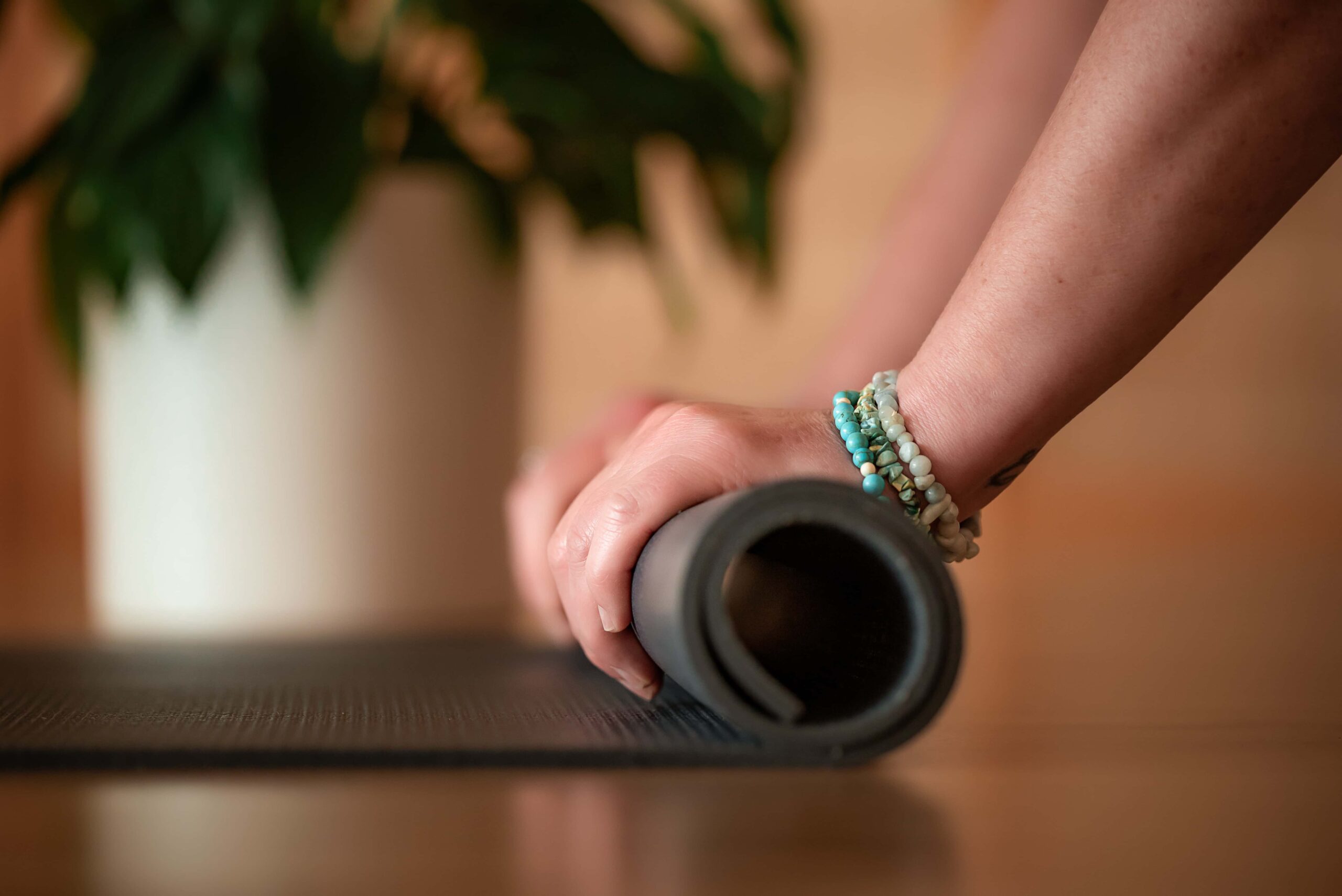 Close up photo of a yoga teacher rolling up her bat with a pot plant in the background
