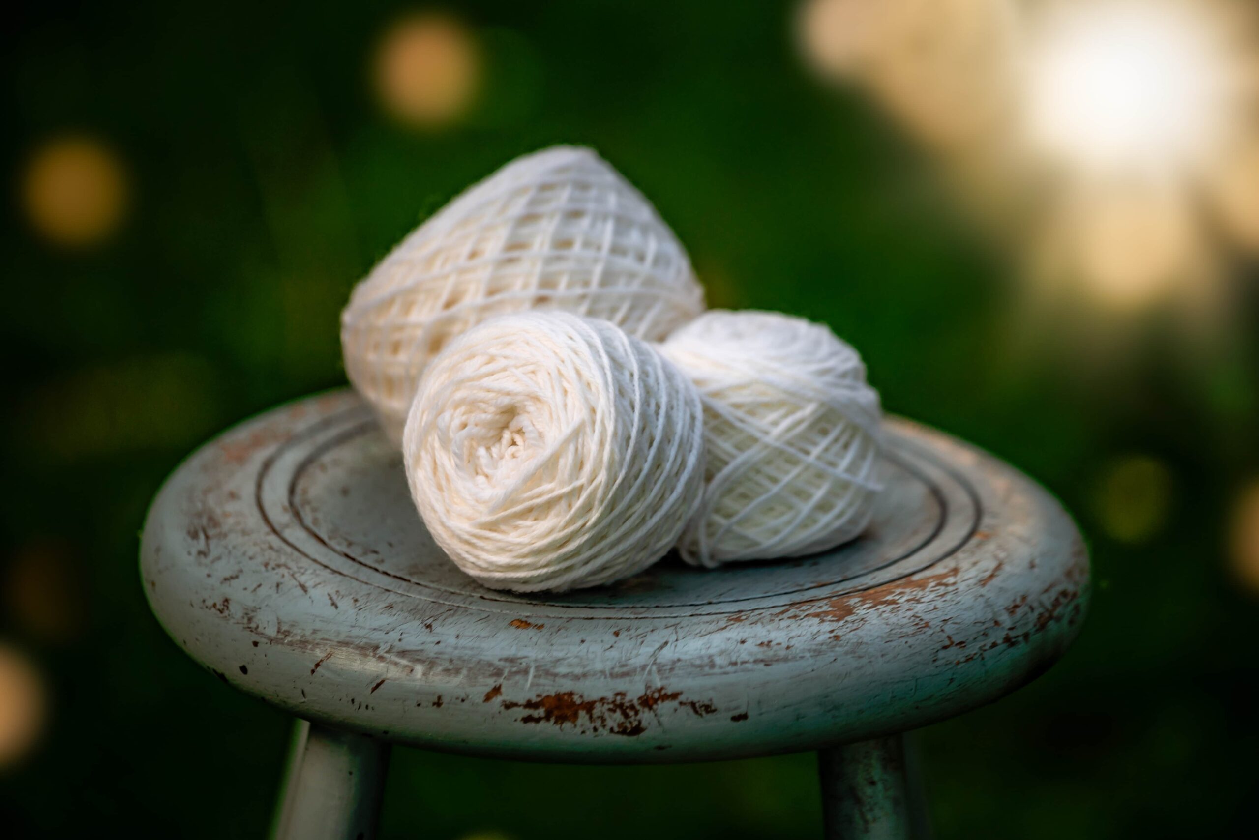 Three balls of white yarn positioned on distressed blue wooden stool as sunsets behind